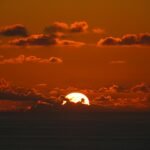 the sun is setting over the ocean with clouds